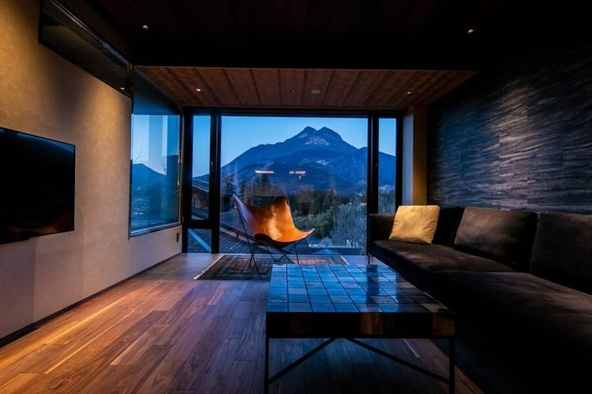 Un salon moderne avec une grande fenêtre, un canapé, un fauteuil et un téléviseur à écran plat.