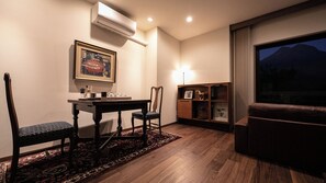 A room with a dining table, chairs, a framed artwork, a lamp, a bookshelf, and a window with a view. - Yufunogo Saigakukan (Yufu)