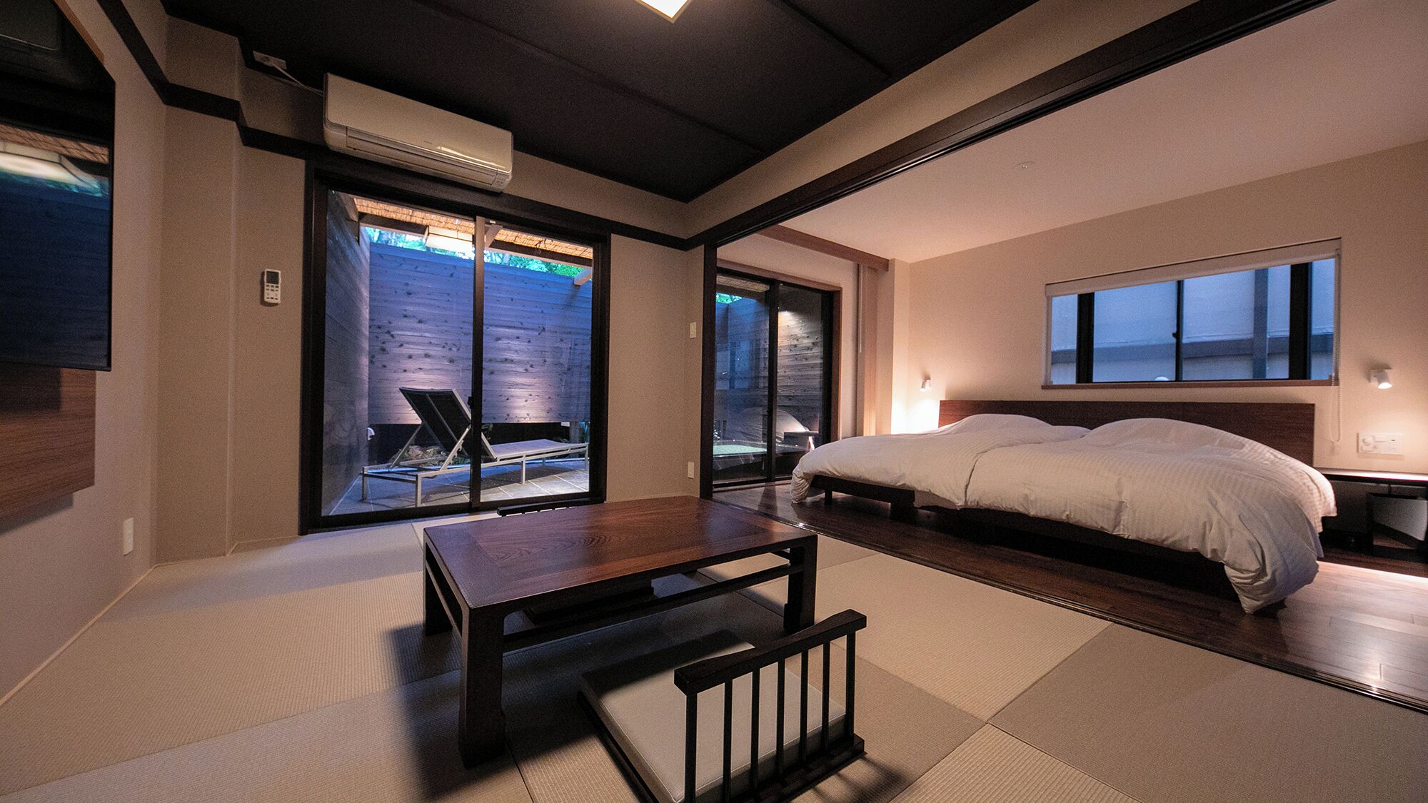 Een moderne slaapkamer met een groot bed, een houten tafel en een schuifdeur naar een buitenruimte.