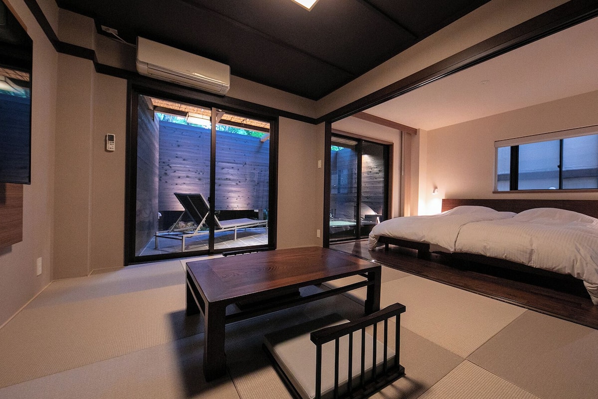 Une chambre moderne avec un grand lit, une table en bois et une porte-fenêtre coulissante donnant sur un espace extérieur.