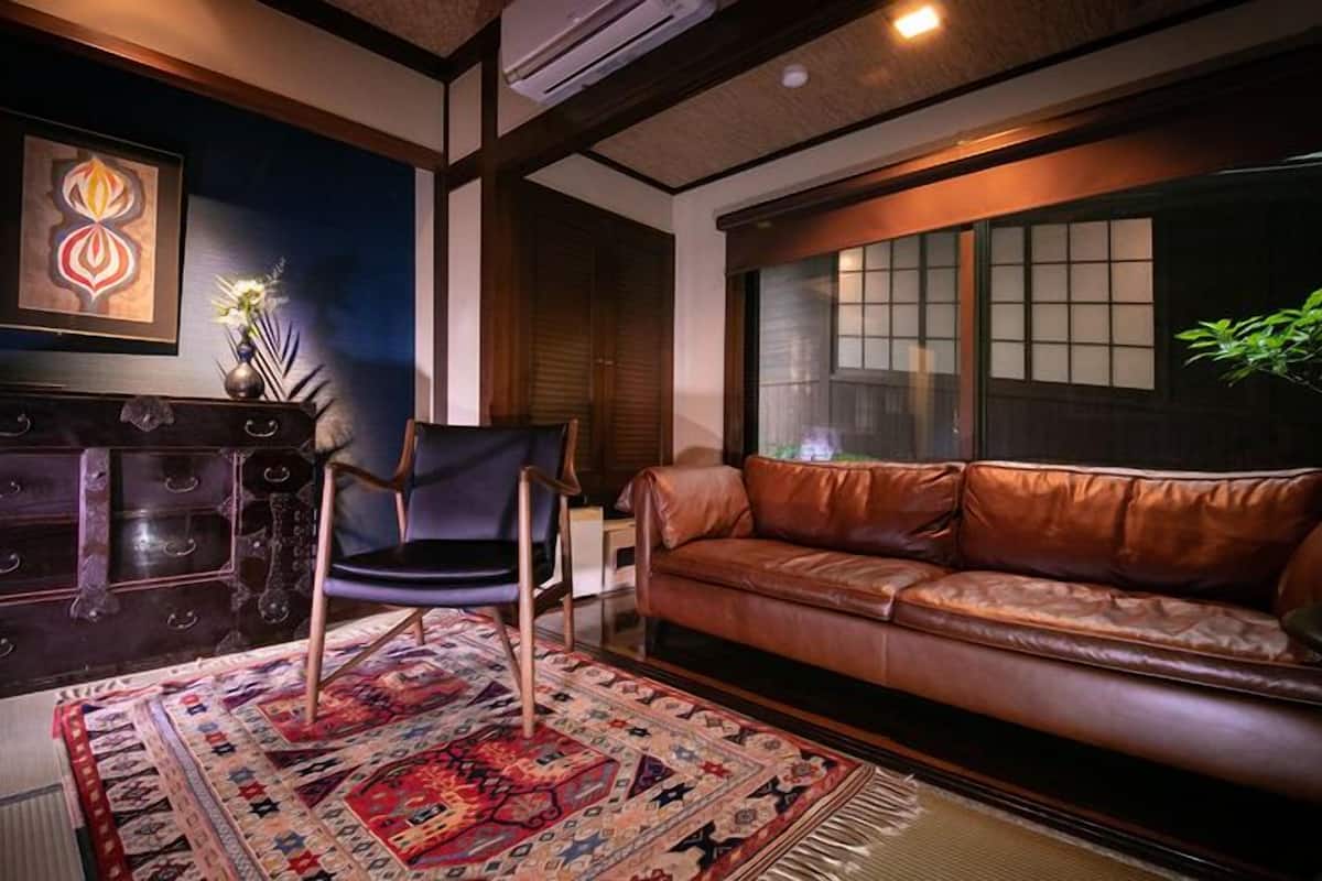 Une pièce avec un canapé en cuir marron, un meuble en bois foncé, un tapis à motifs et un climatiseur fixé au mur.