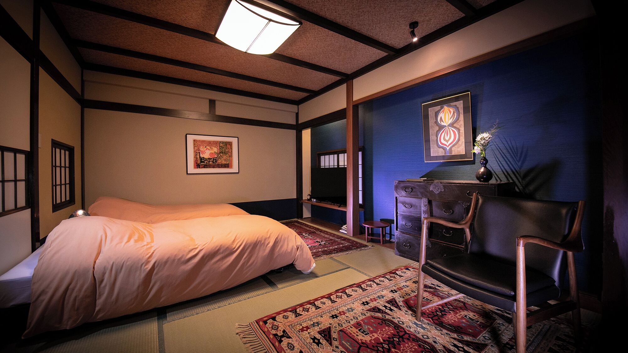 Een traditionele Japanse kamer met tatami vloeren, een laag houten bed, een bureau met stoel en een blauwe accentmuur.