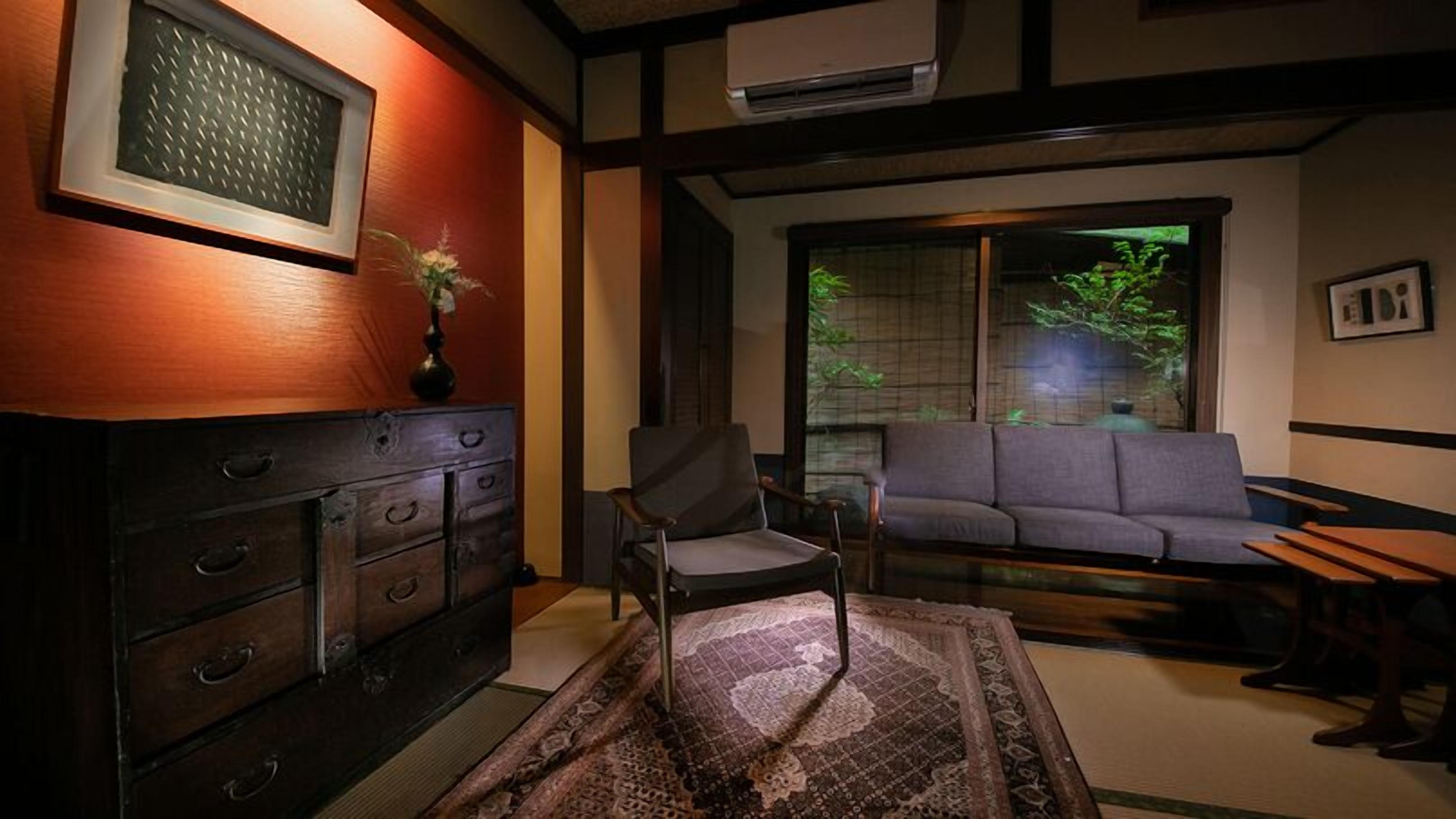 Een traditionele Japanse kamer met tatami vloeren, een lage houten dressoir, een sofa en een schuifdeur die uitkomt op een tuin.