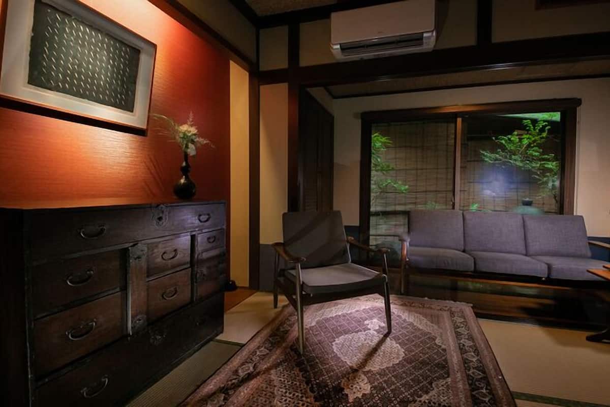 Une pièce de style japonais traditionnel, avec un sol recouvert de tatamis, une commode en bois basse, un canapé et une porte coulissante donnant sur un jardin.