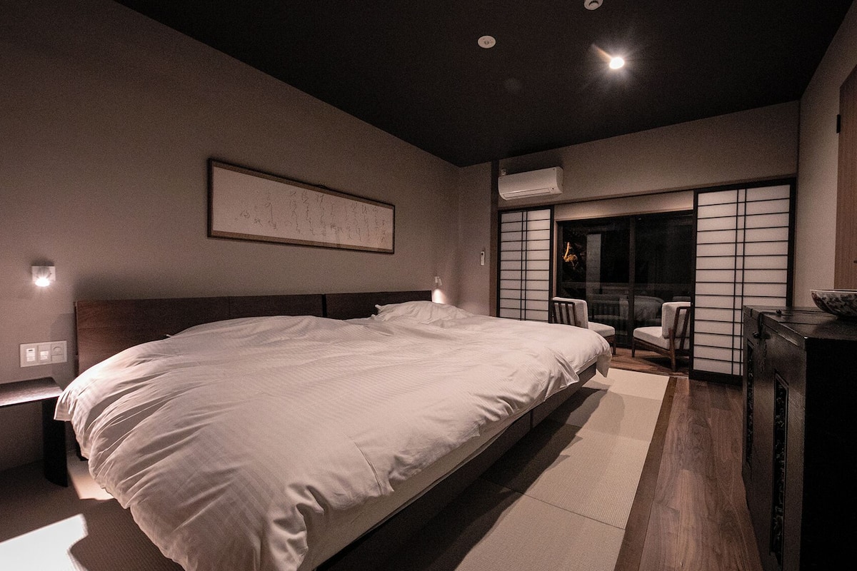 Une chambre d’hôtel moderne dotée d’un grand lit, d’un bureau avec un récipient, et d’une porte coulissante donnant sur un coin salon.