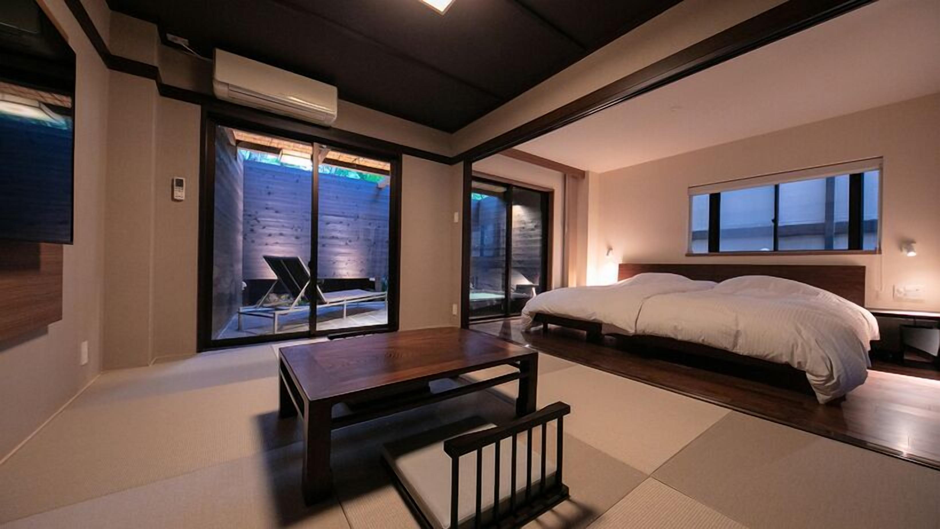 Een moderne slaapkamer met een groot bed, een klein tafeltje en uitzicht op de omgeving via schuifdeuren.