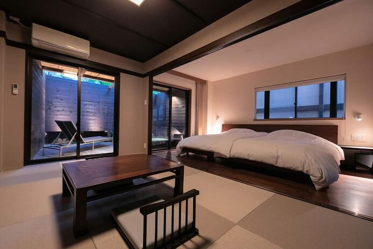 Une chambre moderne avec un grand lit, une petite table et une vue sur l’extérieur grâce à des portes coulissantes.