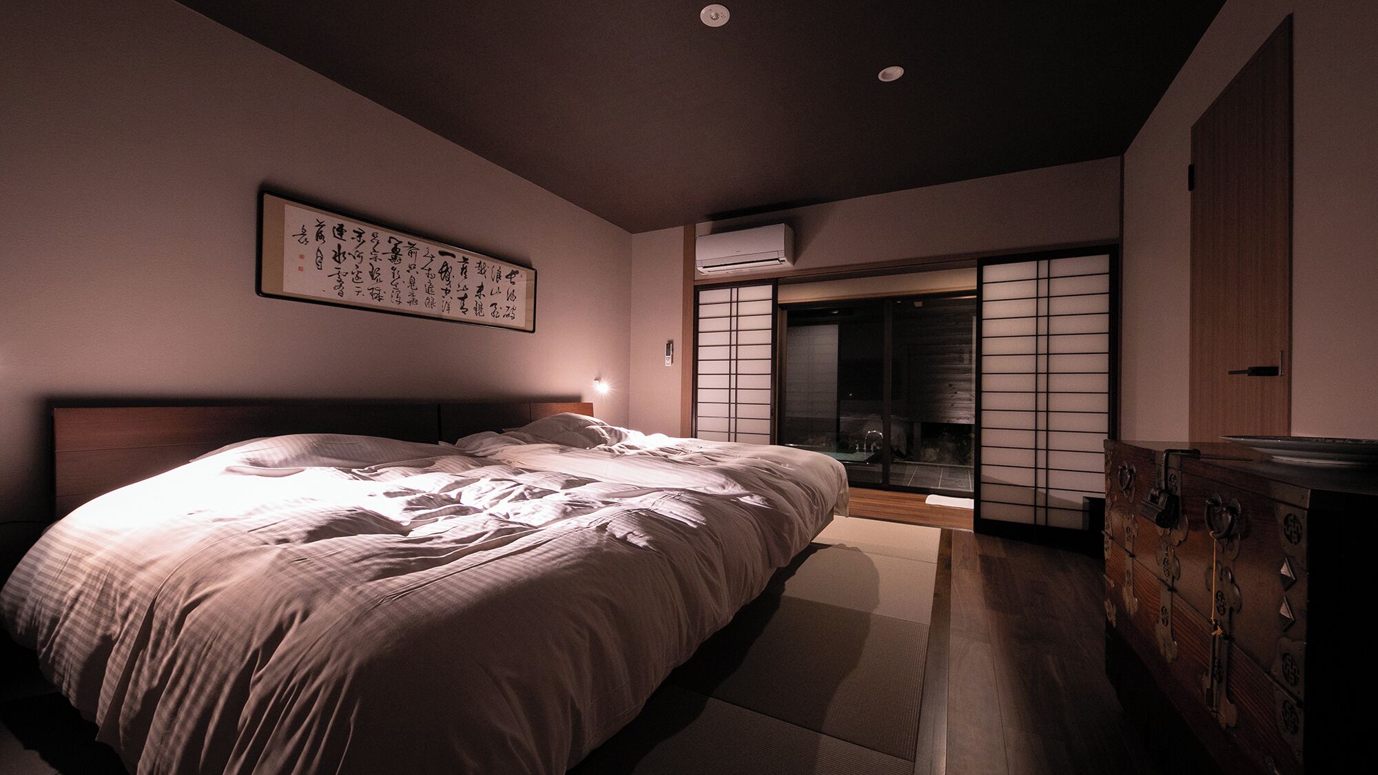 Een slaapkamer met een bed, een wandairconditioner, een schuifdeur van shoji-schermen en een traditionele Japanse kast.