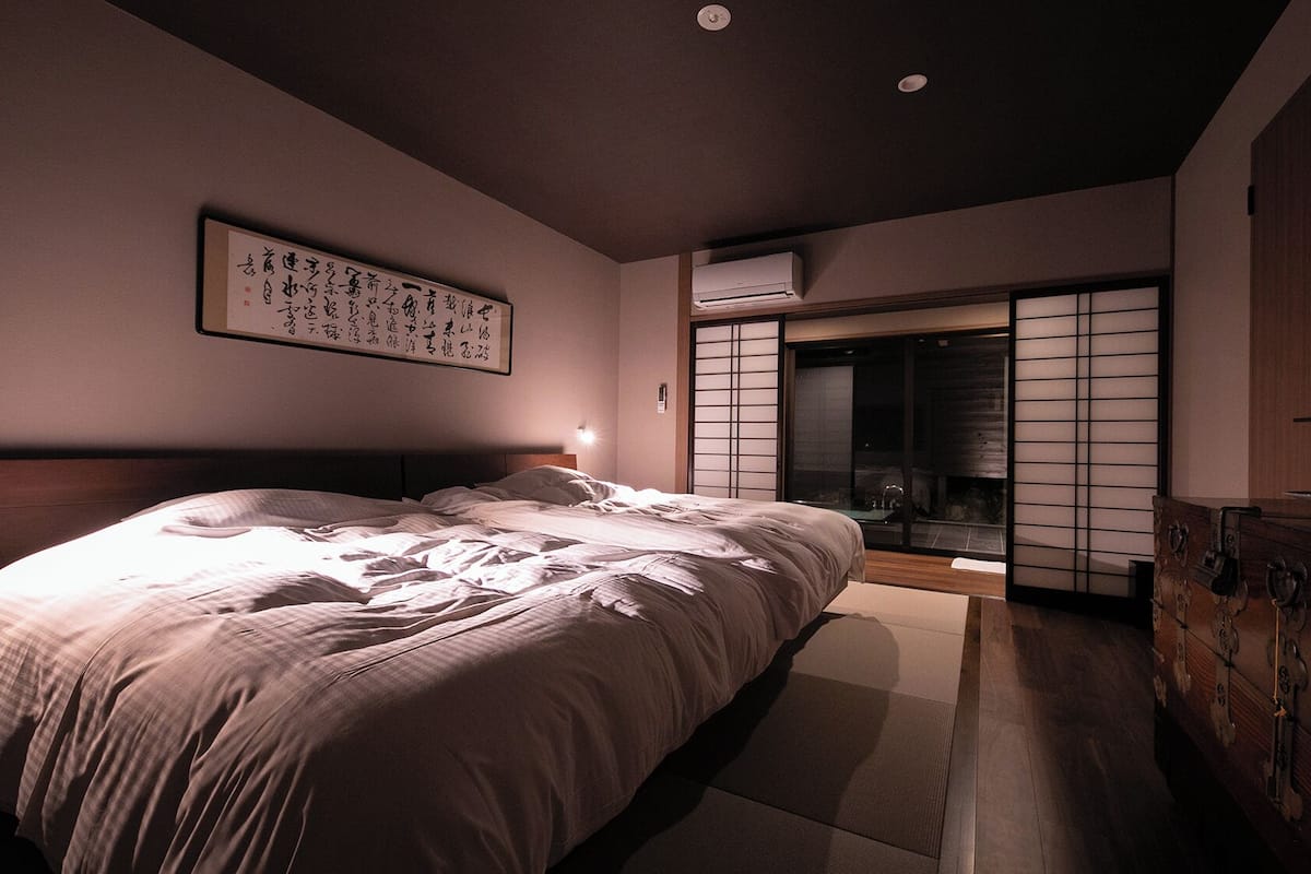 Une chambre comprenant un lit, un climatiseur fixé au mur, une porte-écran coulissante de style japonais (shoji) et un meuble traditionnel japonais.