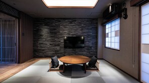 Una habitación moderna con pared de piedra, televisión de pantalla plana, una mesa redonda de madera y esteras de tatami.
