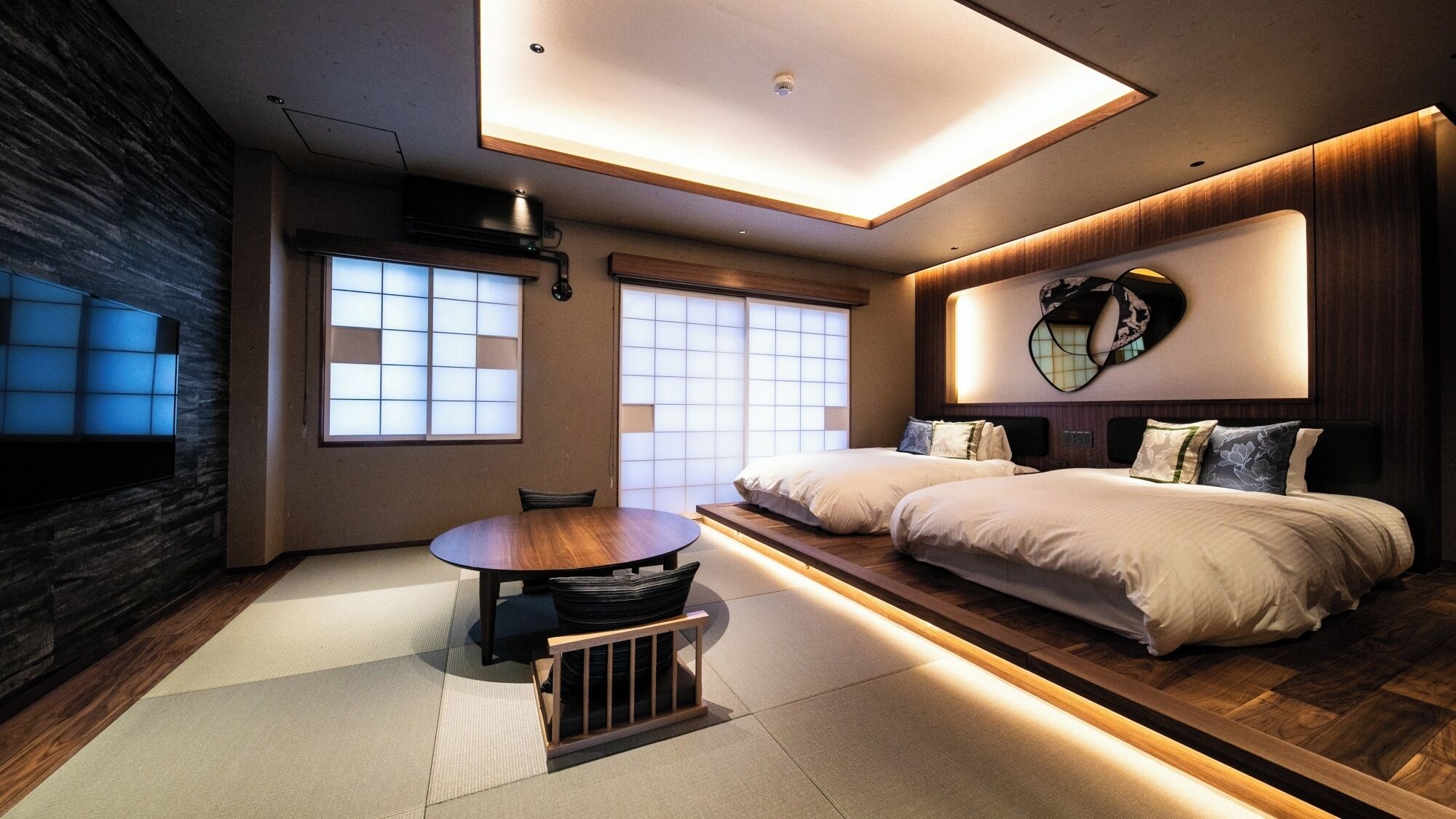 Een moderne hotelkamer met een groot bed, een eettafel en uitzicht op de stad door grote ramen.