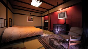A traditional Japanese-style bedroom with tatami flooring, a bed, a dresser, a television, and a chair. - Yufunogo Saigakukan (Yufu)
