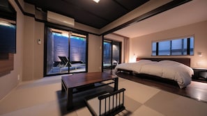 Een moderne slaapkamer met een groot bed, een houten tafel en een schuifdeur naar een buitenruimte.