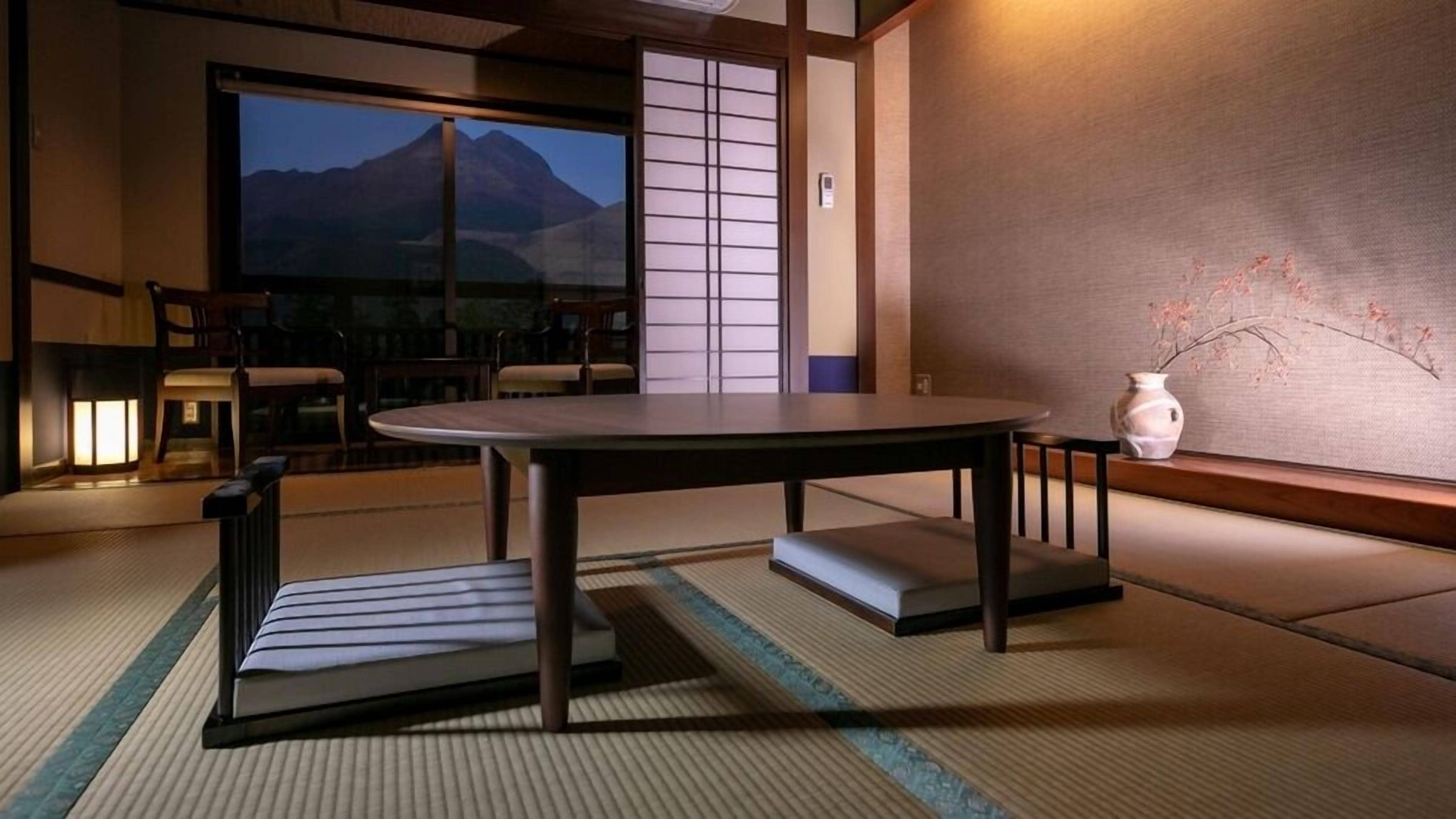 A traditional Japanese room with tatami flooring, a low table, and a view of a mountain.