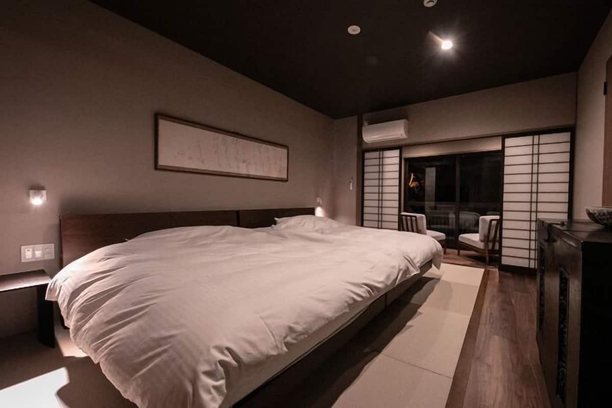 Une chambre moderne avec un grand lit, un bureau avec un bol, et une porte coulissante donnant sur un balcon.