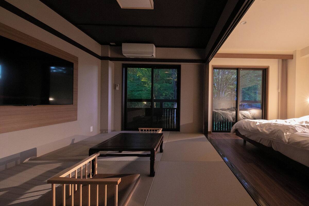 Une chambre à coucher moderne, équipée d’un lit, d’une télévision et d’une porte-fenêtre coulissante donnant sur un balcon.