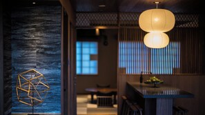 A traditional interior with a geometric light fixture, a sliding door, and a dining area with a table and chairs. - Yufunogo Saigakukan (Yufu)