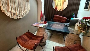 Ein Essbereich mit einem Glastisch, vier gepolsterten Stühlen, einem Wandbehang aus Makramee und einem Spiegel an der Wand.