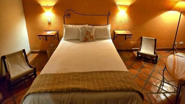Ein Hotelzimmer mit einem großen Bett, zwei Nachttischen, einem Sessel und einer Stehlampe.