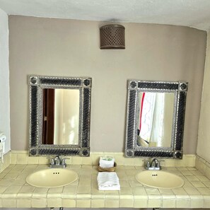Un baño con dos espejos, dos lavabos y una pequeña cesta con una toalla.