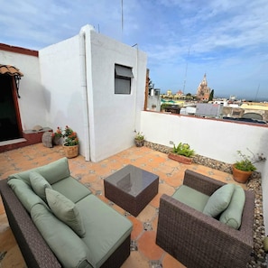 A rooftop patio with outdoor furniture, potted plants, and a view of a historic building in the background.