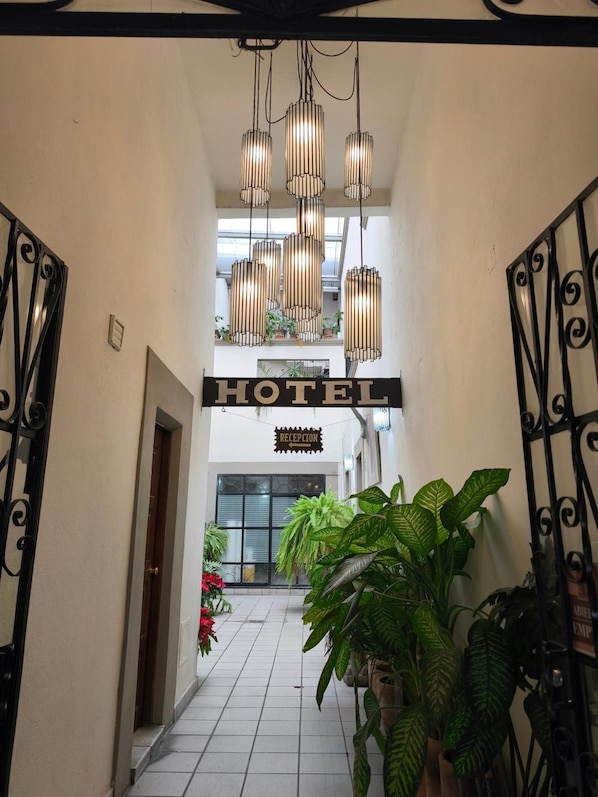 A hotel entrance with a reception desk, a sign indicating the reception area, and a staircase leading to the upper floor.