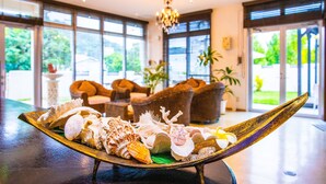 A reception area with a display of seashells on a wooden tray, wicker furniture, and large windows with a view of greenery. - Kerama Terrace (Tokashiki)