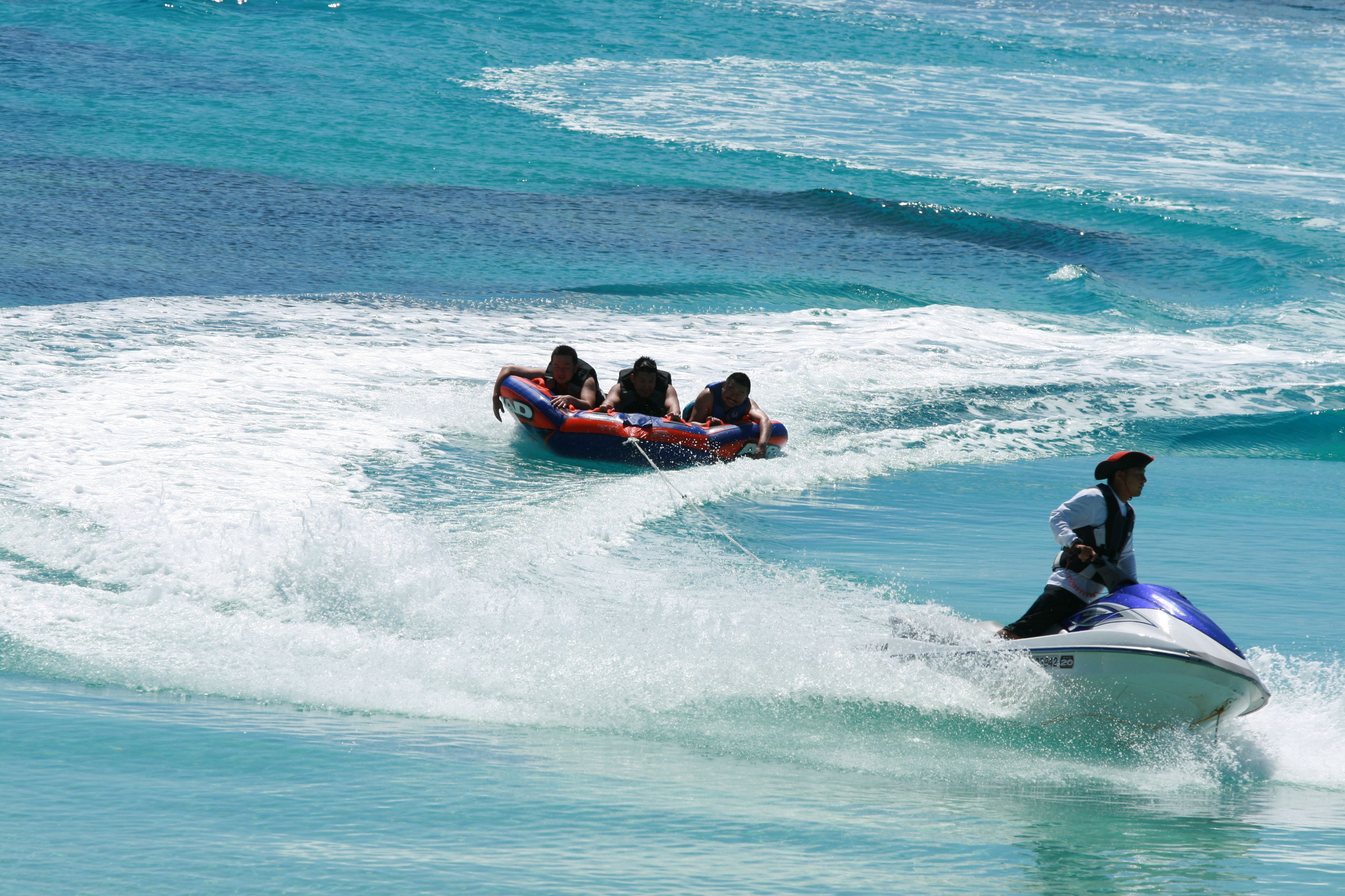 Um jet ski com uma pessoa a usá-lo, e um grupo de pessoas numa jangada na água.