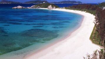 Una playa con aguas turquesas cristalinas, una orilla de arena blanca y colinas verdes al fondo.