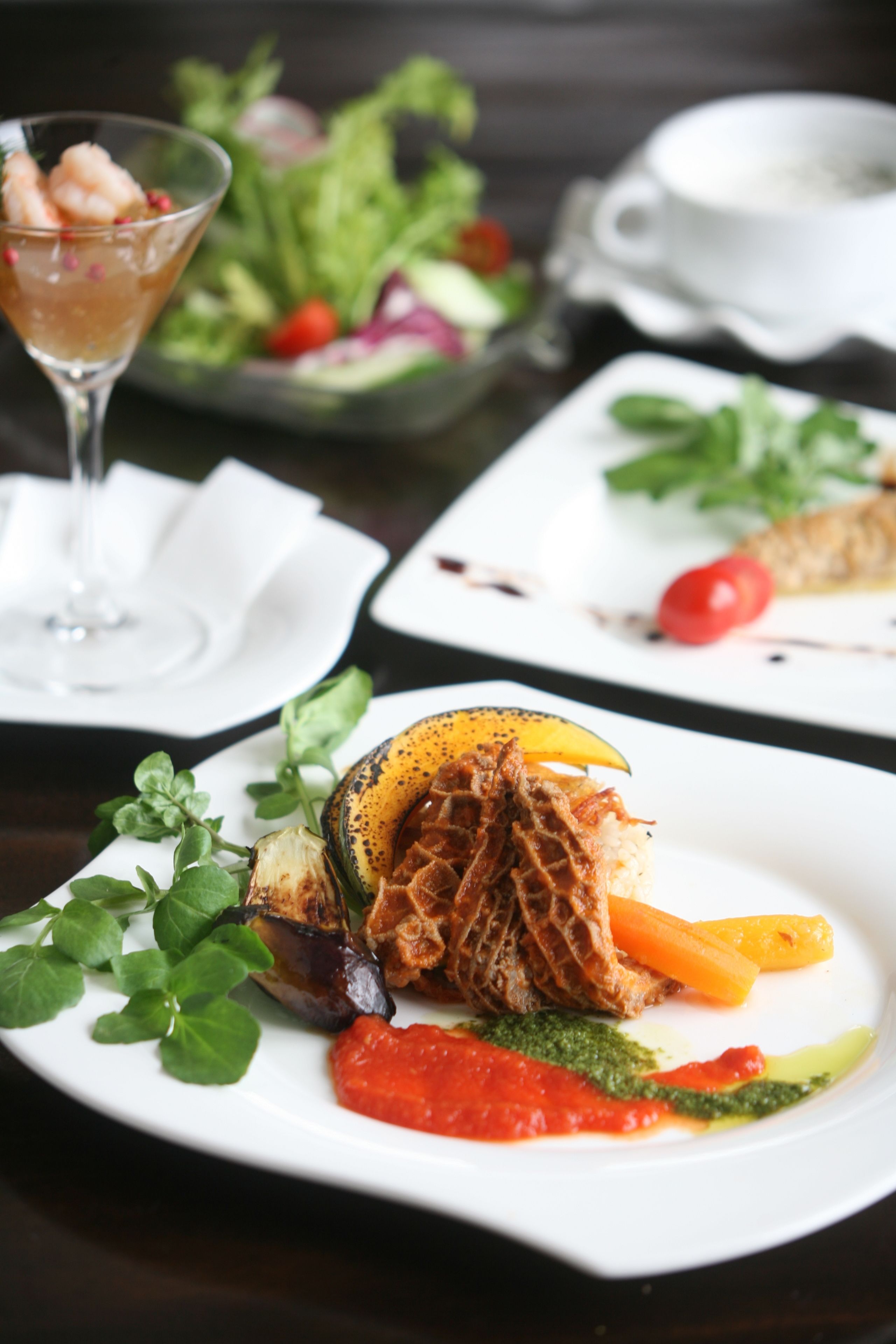 A dining table with plates of food, a glass of drink, and a bowl of salad.