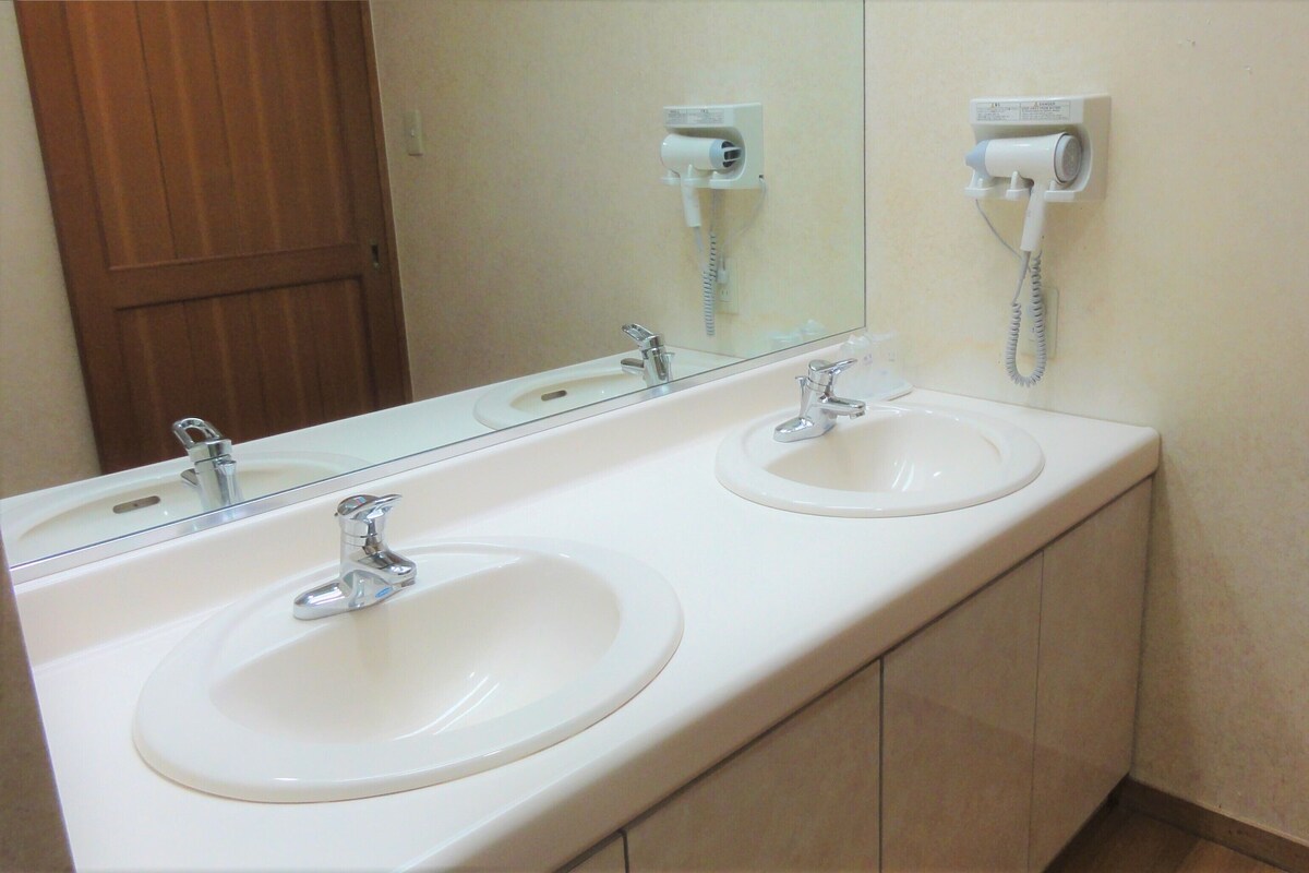 A bathroom with two sinks, a mirror, and a hairdryer mounted on the wall.
