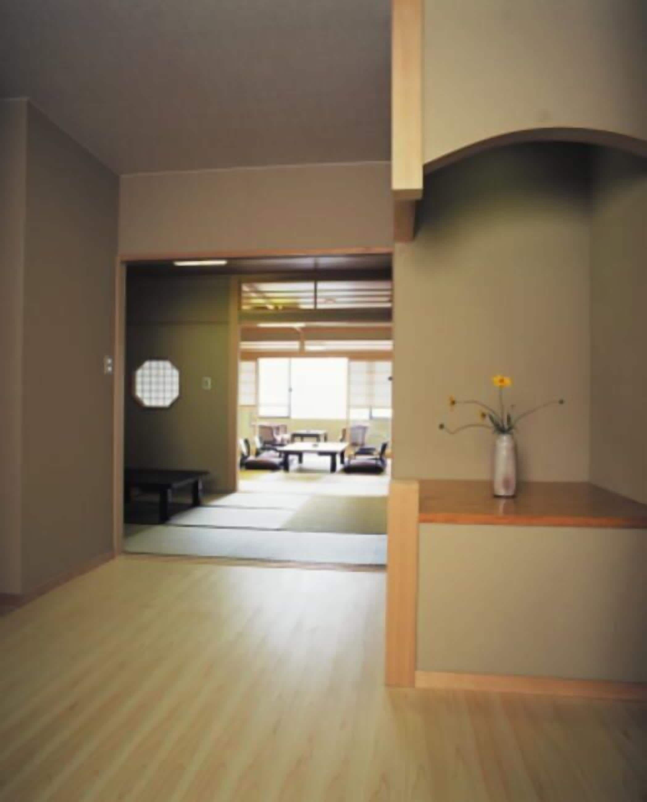 Amplia habitación con piso de madera, una pequeña mesa de madera con un florero, y vista hacia un comedor con una mesa baja y sillas.