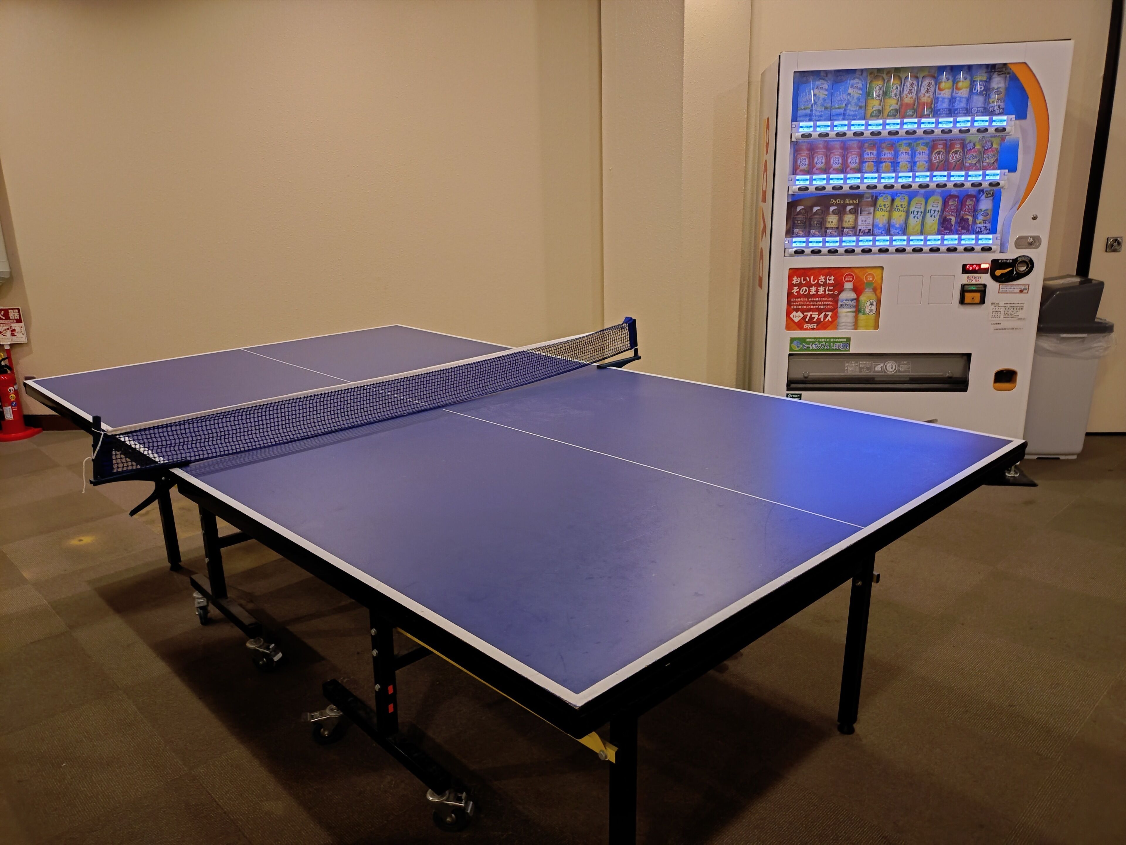 A ping pong table with a net in a room with a vending machine.