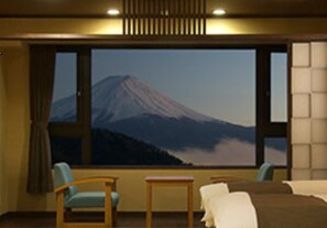 Une chambre d’hôtel dotée d’une grande fenêtre donnant sur une montagne. La chambre contient deux fauteuils et une petite table.
