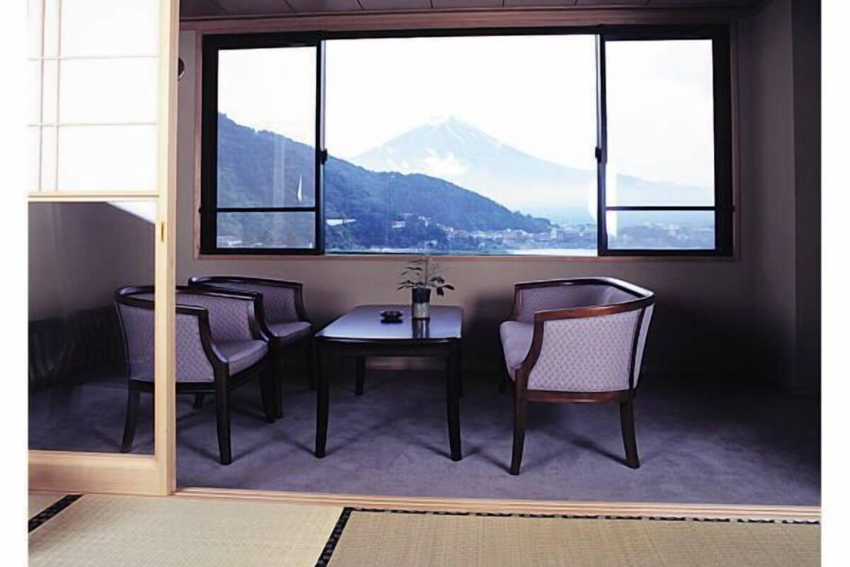 A room with tatami flooring, a low table with chairs, and a large window offering a mountain view.