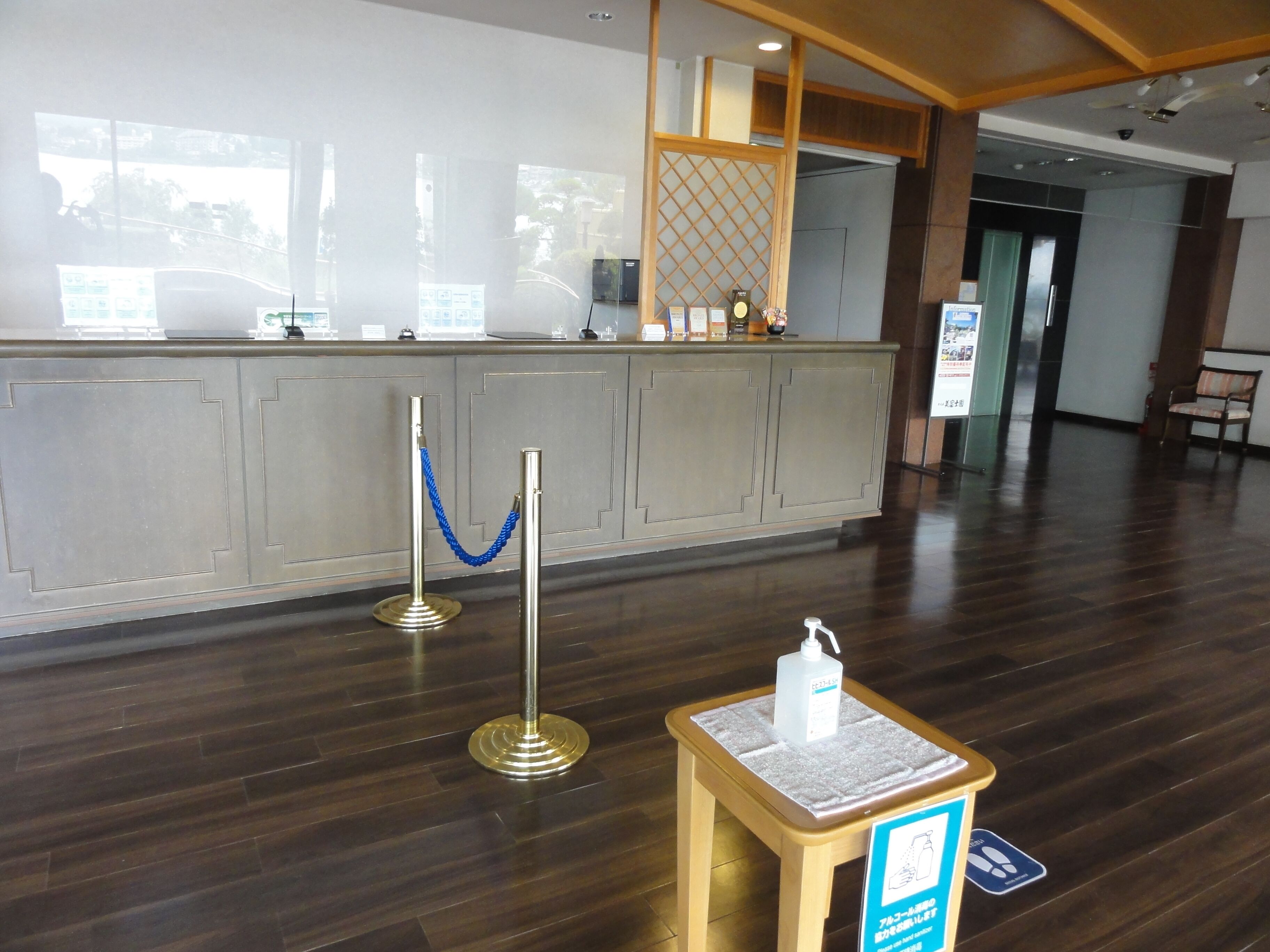 A reception area with a wooden reception desk, a blue rope barrier, and a sign with a hand sanitizer dispenser.