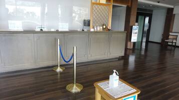 Zona de recepción con un mostrador de madera, una barrera de cuerda azul y un dispensador de gel hidroalcohólico.