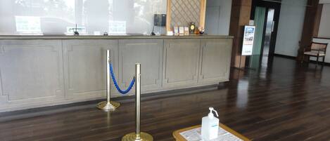 A reception area with a wooden reception desk, a blue rope barrier, and a sign with a hand sanitizer dispenser.