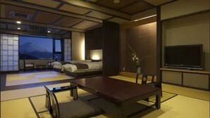 A traditional Japanese-style room with tatami flooring, a low table, a sofa, and a TV. - Hotel Mifujien (Fujikawaguchiko)