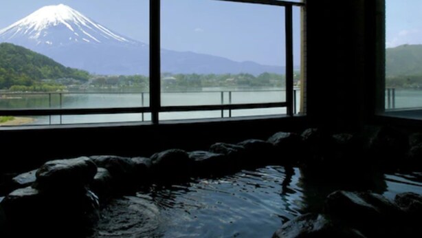 A room with a large window offering a view of a snow-capped mountain and a lake. - Hotel Mifujien (Fujikawaguchiko)