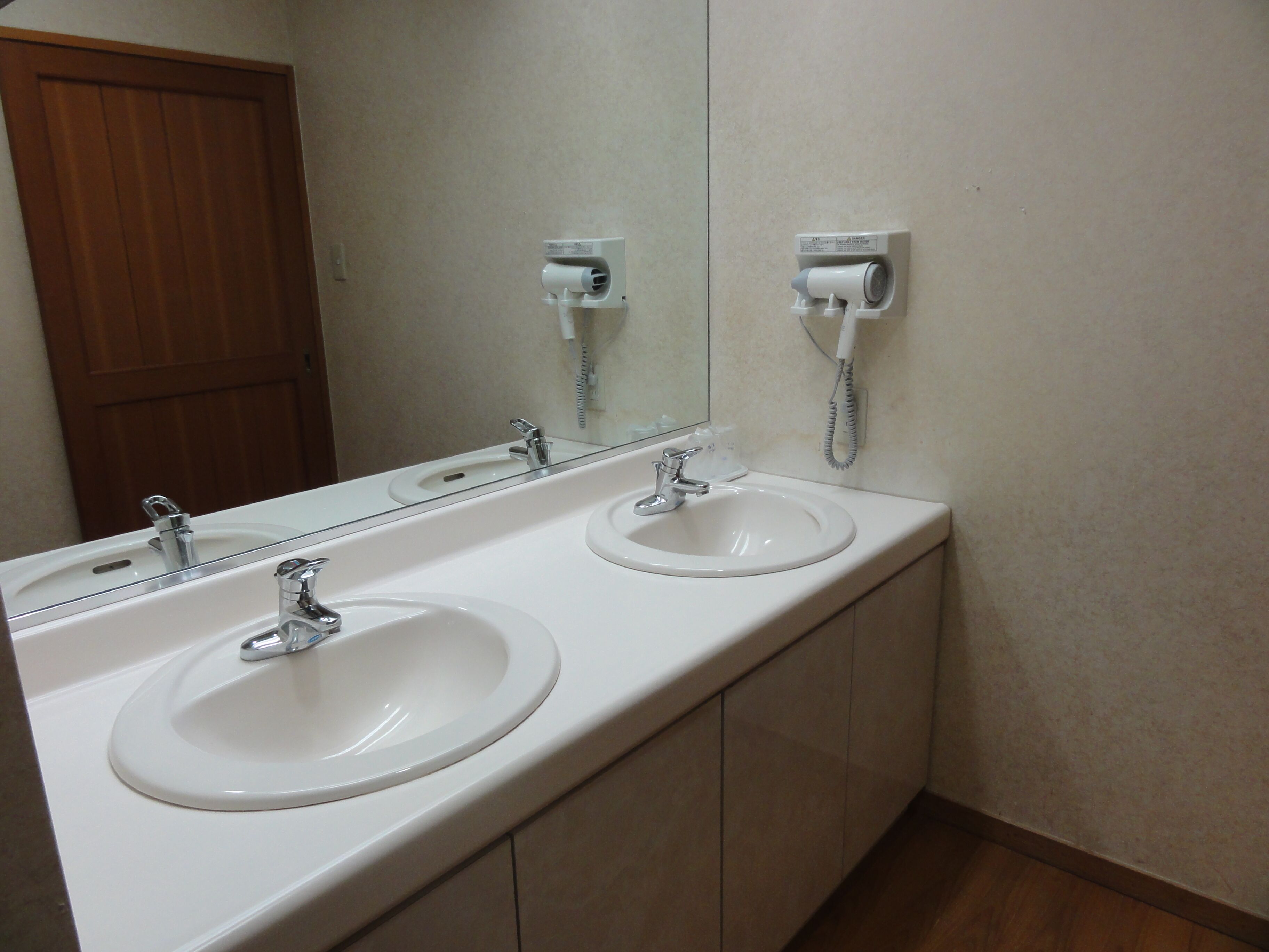 A bathroom with two sinks, a mirror, and a towel dispenser.