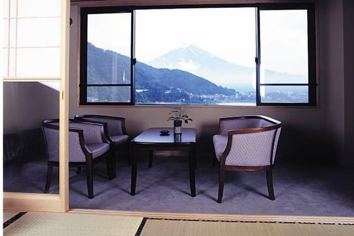 A room with tatami flooring, a low table with chairs, and a large window offering a mountain view.