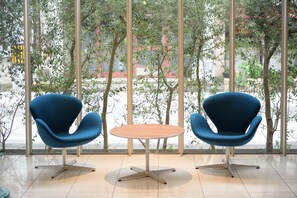 A modern room with two blue chairs and a round table, large windows with a view of trees and buildings. - 7days Hotel Plus (Kochi)