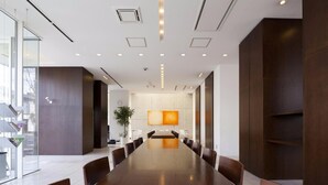 Un salón de conferencias con una larga mesa, sillas, una planta en maceta y una pantalla grande instalada en la pared.