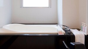 Et badeværelse med et stort badekar, et vindue og toiletartikler på bordet.
