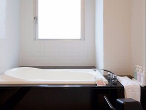 Un baño con una bañera grande, una ventana y artículos de aseo en la encimera.