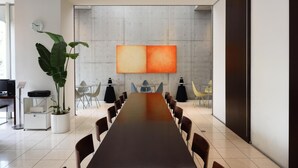 Un salón de conferencias con una larga mesa, sillas, una planta en maceta, un reloj y un cuadro abstracto grande en la pared.