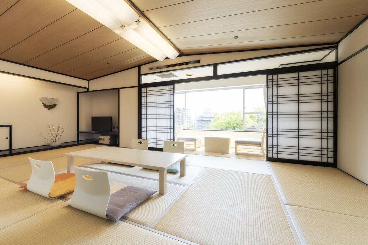 A tatami mat room with a low table, chairs, a TV, and sliding doors.