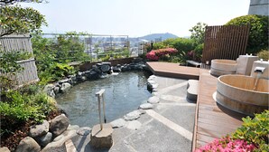 A traditional Japanese onsen with a stone bath, wooden deck, and surrounding greenery. - Chaharu (Matsuyama)