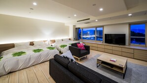 A modern bedroom with a large bed, a sofa, a TV, and a window with a city view. - Chaharu (Matsuyama)